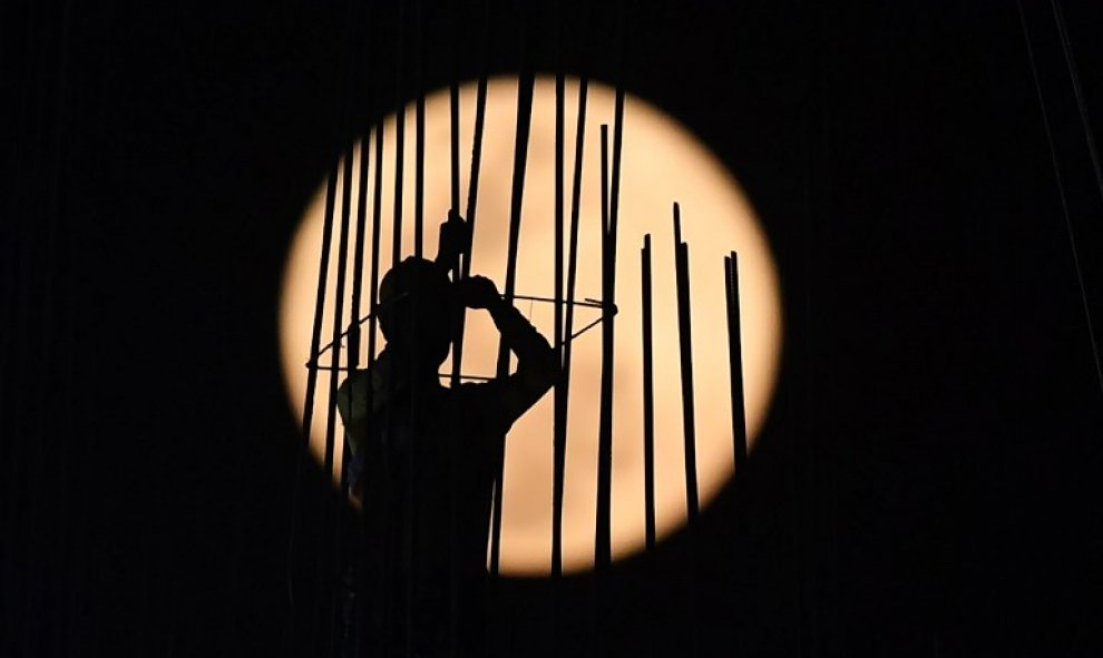 La luna de nieve se eleva cuando un obrero de la construcción trabaja en una obra en Kolkata, la India | AFP/ Dibyangshu Sarkar