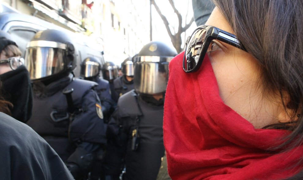 Una mujer mira hacia los agentes antidisturibios de la Policía Nacional presenciados en la inmediaciones de la calle Argumosa de Madrid, donde se manifestan activistas de la plataforma 'Stop Desahucios' ante la previsión de varios desahucios decretados p