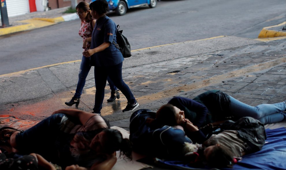 Dos mujeres caminan por la calle mientras las migrantes de América Central duermen en el suelo en el Parque Central Miguel Hidalgo, en México. / Reuters