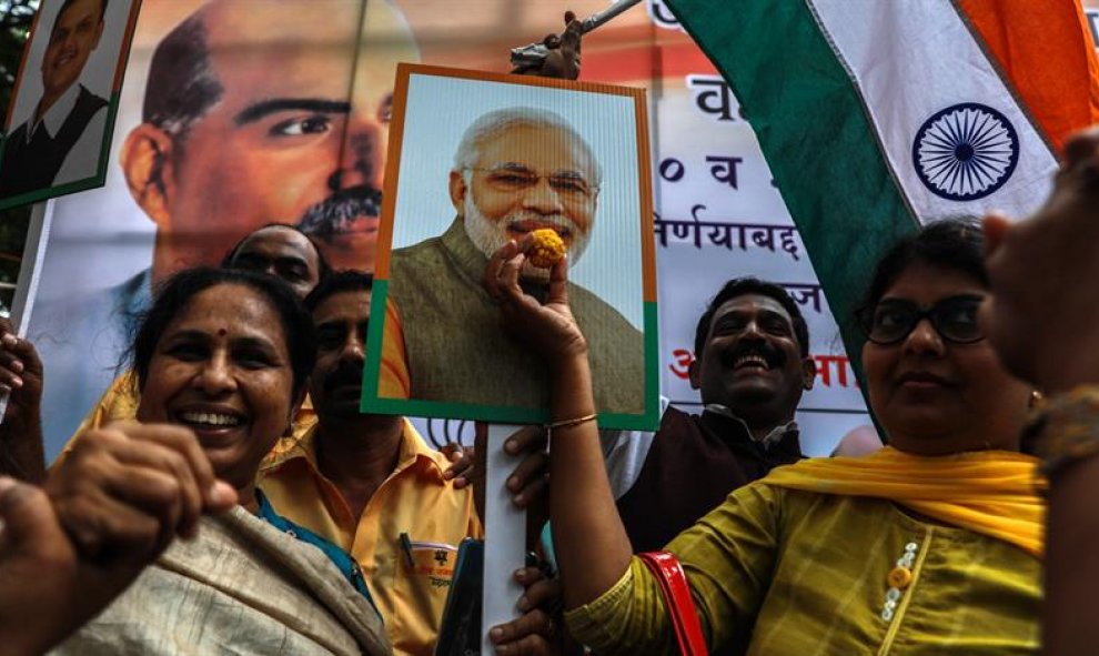 Los partidarios del partido indio Bharatiya Janata (BJP) sostienen la bandera nacional india y el cartel del primer ministro indio Narendra Modi, gritan consignas y distribuyen dulces mientras celebran la eliminación del artículo 370 | EFE