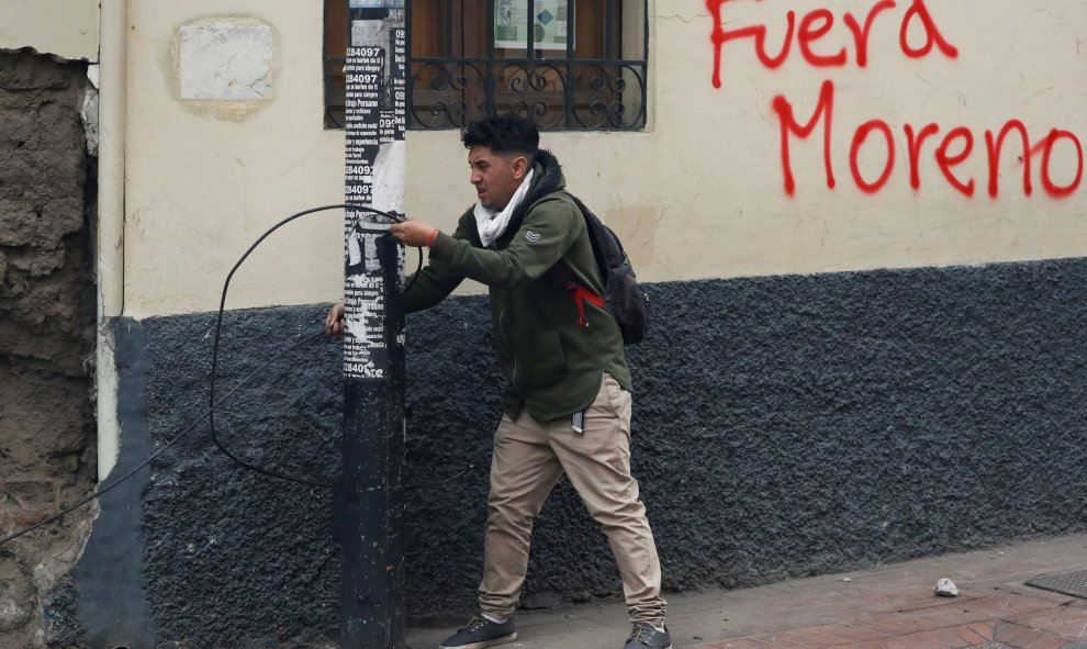 Un manifestante tira de un cable al lado de un graffiti donde se puede leer 'Moreno fuera'. REUTERS/Carlos Garcia Rawlins