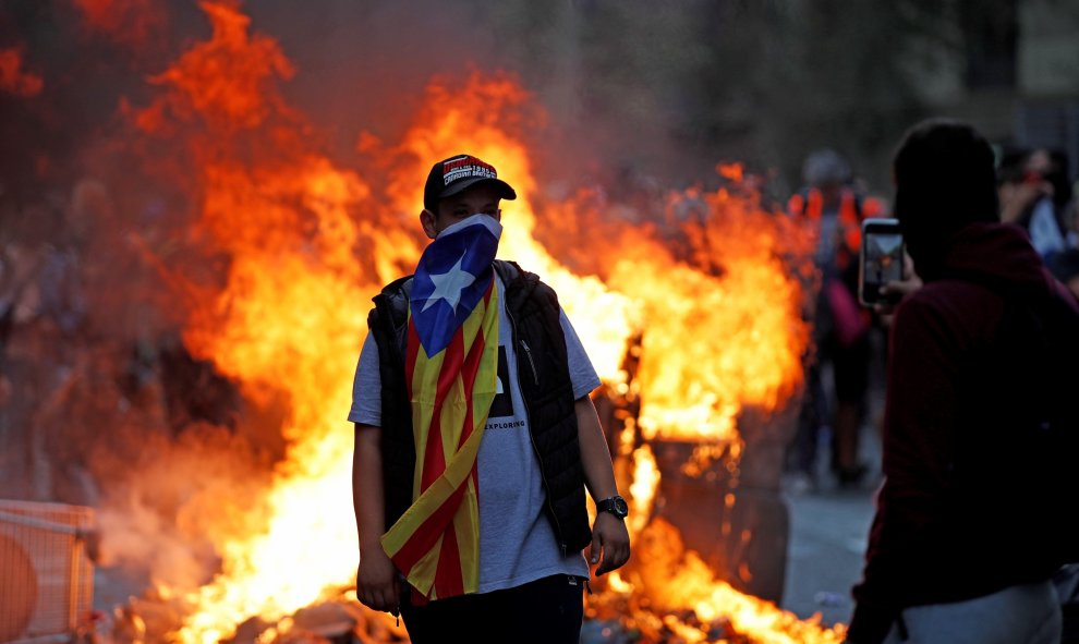 Un manifestante cubierto con la estelada camina con el fuego de las barricadas al fondo. / EFE