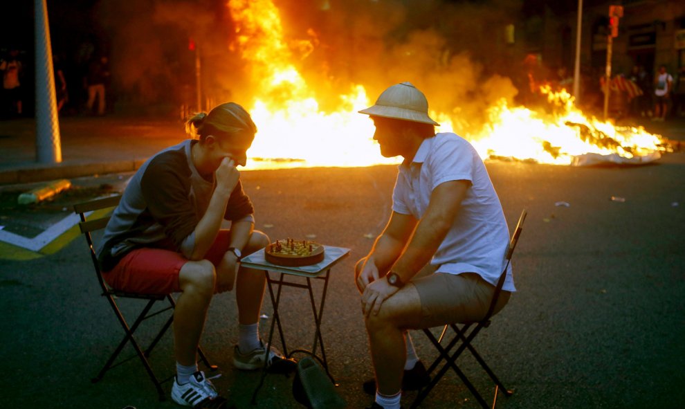 Dos hombres bromean jugando al ajedrez en medio de los disturbios que se están produciendo en Barcelona. /EFE