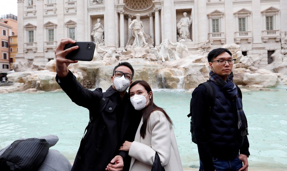 Turistas fotografiándose en la Fontana de Trevi con mascarillas protectoras para evitar el contagio por coronavirus. REUTERS