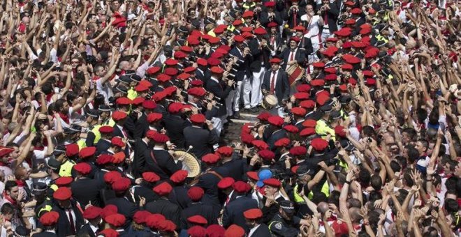 Cientos de personas alzan sus brazos al son de la música de los gaiteros que salen desde el Ayuntamiento de Pamplona para amenizar las calles del Casco Viejo de la ciudad tras el lanzamiento del tradicional chupinazo que ha abierto a las doce del mediodía