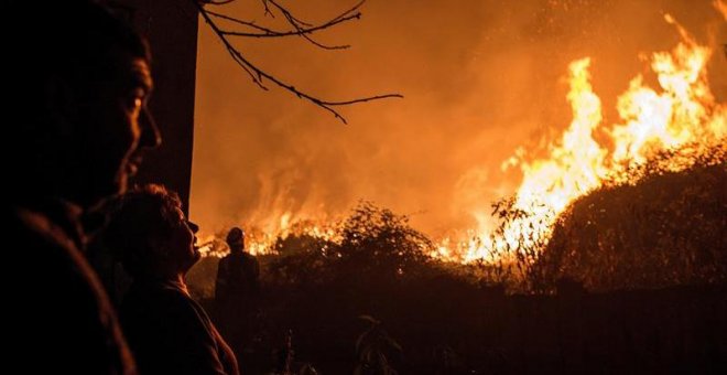 Los incendios están afectando especialmente a Galicia, donde han muerto cuatro personas. En la imagen, unos vecinos observan como se acerca a sus casas el incendio forestal de Carballeda de Avia (Ourense). - EFE