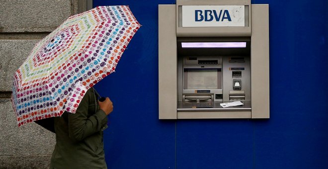 Una mujer con paraguas junto a un cajero automático de una sucursal de BBVA en Madrid. REUTERS/Andrea Comas