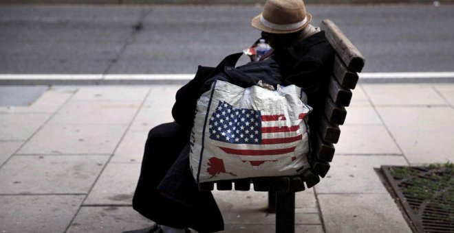 Una mujer sin hogar descansa en un banco.- AFP