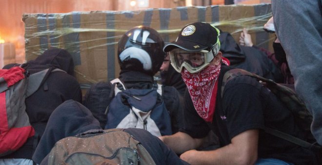 Varios jóvenes encapuchados se protegen de las balas de goma con un parapeto de cartón y cinta de embalaje, durante los disturbios de Barcelona. GUILLEM SANS