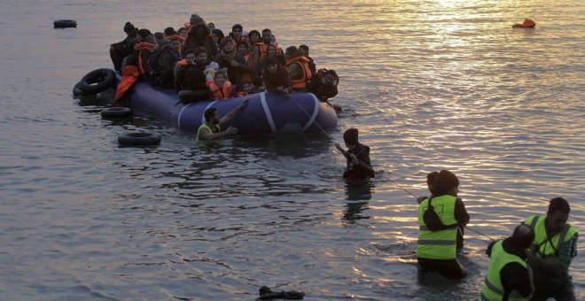 Voluntarios de una ONG ayudan a refugiados y migrantes que llegan en una lancha neumática a la costa de Mytilini, en la isla de Lesbos (Orestis Panagiotou / EFE)