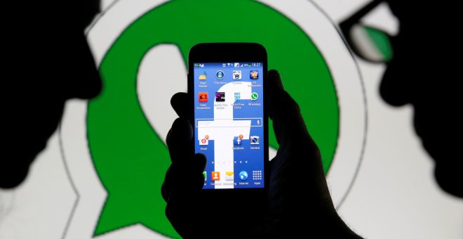 Foto que muestra un hom,bnre sosteniendo un móvil con el logo de Facebook en la pantalla, y detrás, el logo de logo de WhatsApp. REUTERS/Dado Ruvic