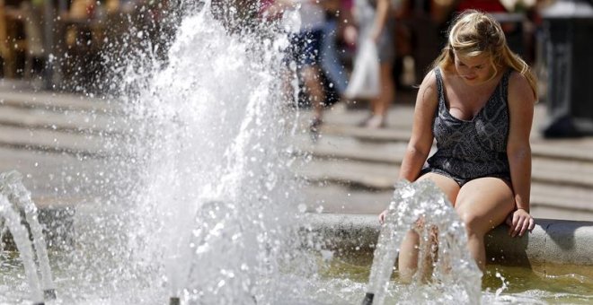 Una turista se refresca en la fuente de la plaza de la Virgen de Valencia. /EFE