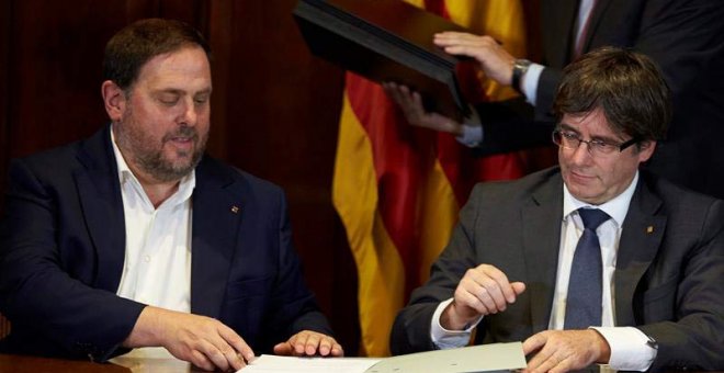 El presidente de la Generalitat, Carles Puigdemont (derecha), acompañado por el vicepresidente Oriol Junqueras, firma la convocatoria de referéndum. | ALEJANDRO GARCÍA (EFE)