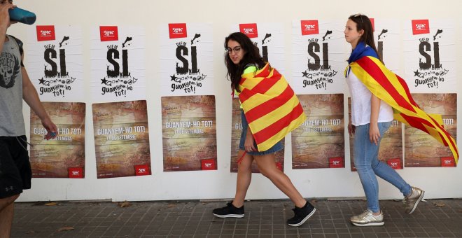 Jóvenes llevan banderas de Catalunya a su paso por una pared con pósters de apoyo al referéndum soberanista en el día de La Diada /REUTERS (Albert Gea)