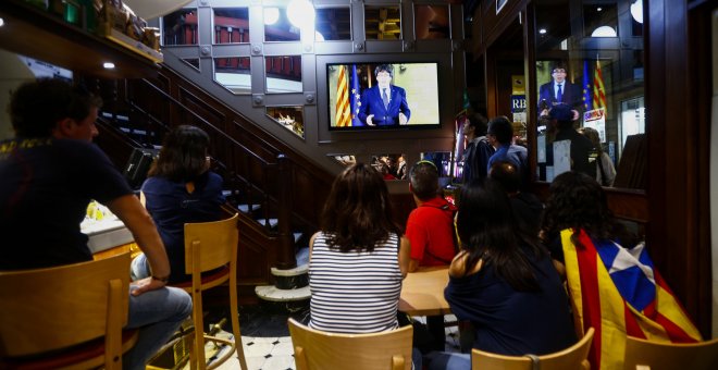 Un grupo de ciudadanos siguen desde una pantalla de televisión la declaración institucional del presidente de la Generalitat, Carles Puigdemont, tras la decisión del Gobierno de aplicar el artículo 155 en Cataluña. EFE/Quique García