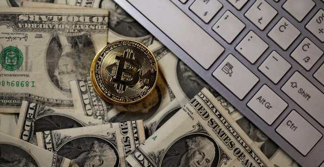 Un bitcoin sobre varios billetes de dolares americanos./REUTERS