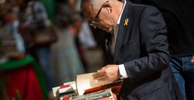 Un hombre con un lazo amarillo en la solapa de su chaqueta hojea un libro en una de las paradas de las Ramblas de Barcelona. / EFE