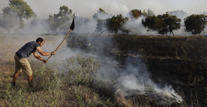 Un hombre apaga un incendio en Kibbutz de Kissufim, a lo largo de la frontera con la Franja de Gaza,  provocado por material inflamable adherido a un globo de helio. / AFP - MENAHEM KAHANA