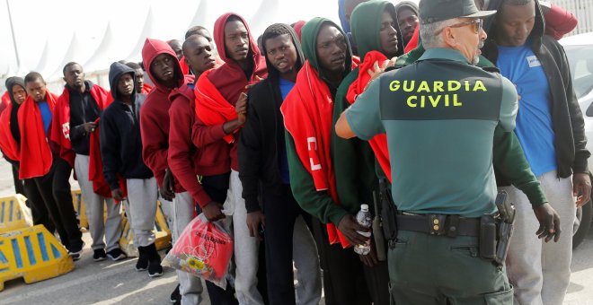 Migrantes parados por un guardia civil antes de ser distribuidos en autobuses - REUTERS