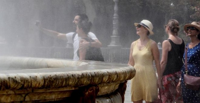 Turistas se refrescan en una fuente céntrica de Sevilla durante la ola de calor que azota España. / EFE
