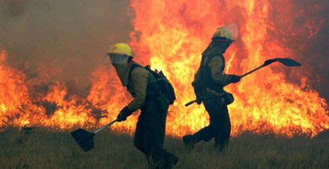 Fotografía de archivo de dos bomberos intentando controlar un incendio forestal en Galicia. EFE