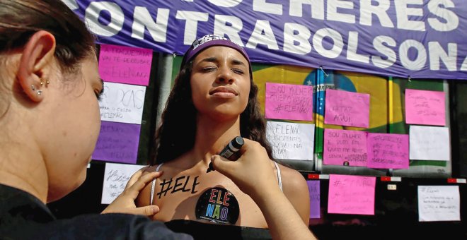 Una mujer pinta en la piel de otra: 'Él no', durante las manifestaciones contra Bolsonaro este sábado en Sao Paulo. REUTERS