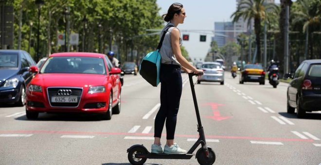 Una joven cruza un paso de peatones con un patinete eléctrico.