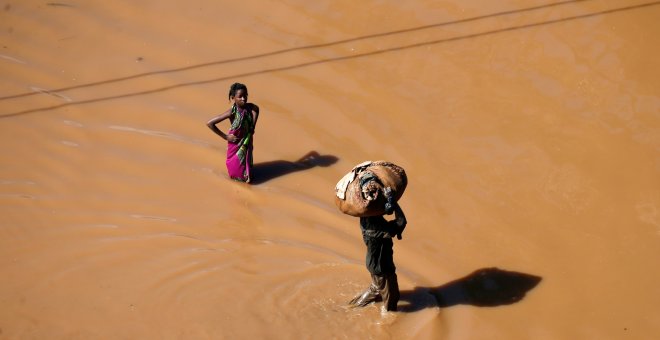 Una niña se detiene para mirar mientras un hombre pasa caminando con el equipaje en la cabeza después del ciclón. Reuters