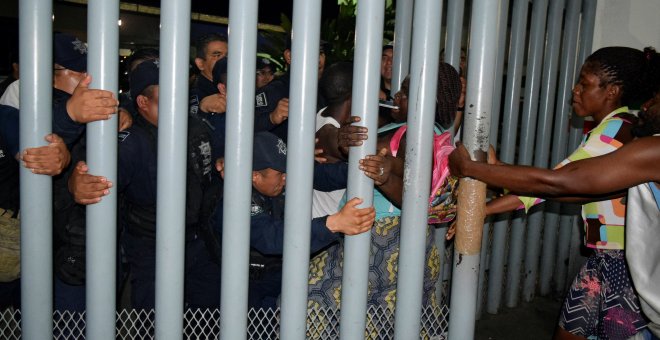 Un grupo de migrantes tiran de la valla del Instituto Nacional de Migración (INM) mientras los policías federales los bloquean durante una protesta en México. | Reuters