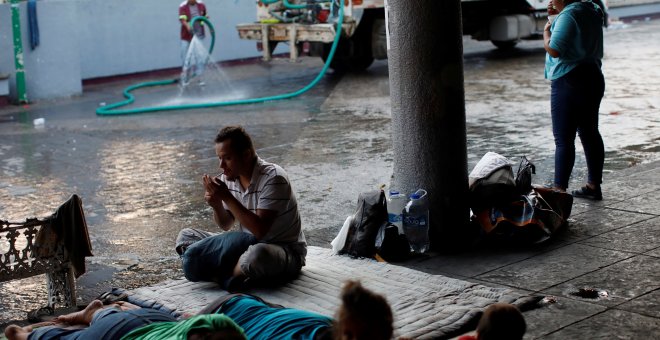 Un trabajador municipal riega la calle mientras los migrantes de América Central duermen en el suelo del parque central Miguel Hidalgo, México. / Reuters