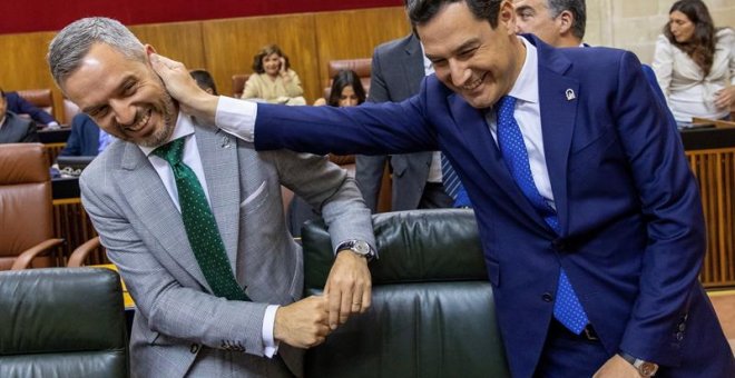 El presidente andaluz, Juanma Moreno, bromea con el consejero de Hacienda, Juan Bravo, al inicio del pleno del Parlamento de Andalucía. /EFE