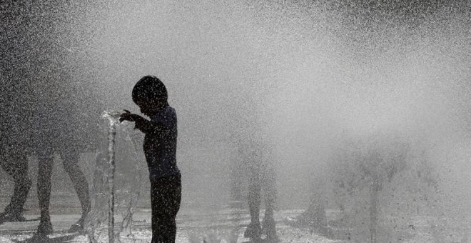 Varios jóvenes combaten las altas temperaturas refrescándose en una fuente de Pamplona. EFE/Villar López