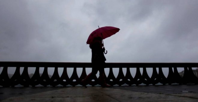 Una mujer camina bajo la lluvia por el paseo marítimo de A Coruña.- EFE