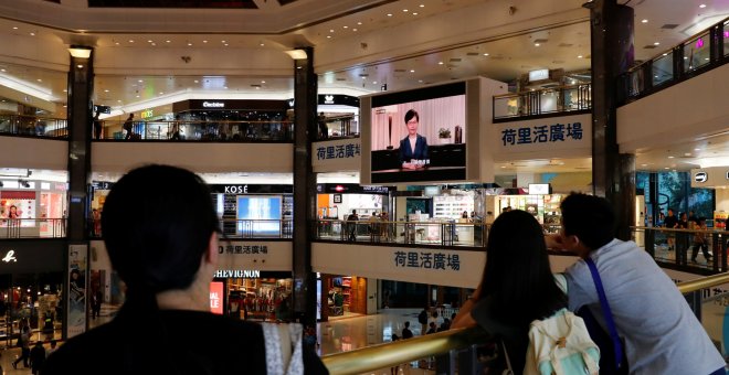 Varias personas escuchan el mensaje televisado de Carrie Lam en un centro comercial de Hong Kong. - REUTERS
