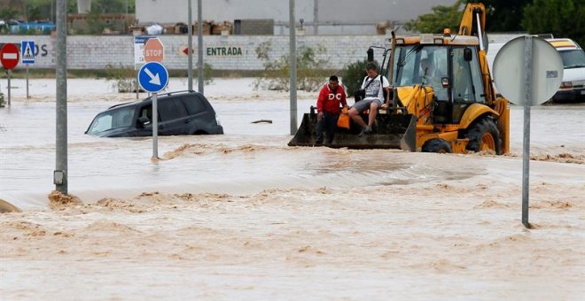 Dos ocupantes de un vehículo son rescatados con una pala mecánica, mientras la carretera permanece inundada por el efecto de las riadas, este viernes, en la ciudad alicantina de Orihuela, que se encuentra incomunicada, a causa del desbordamiento del río
