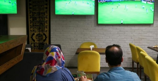 Una mujer ve un partido de fútbol junto a un amigo en una cafetería de Irán. REUTERS