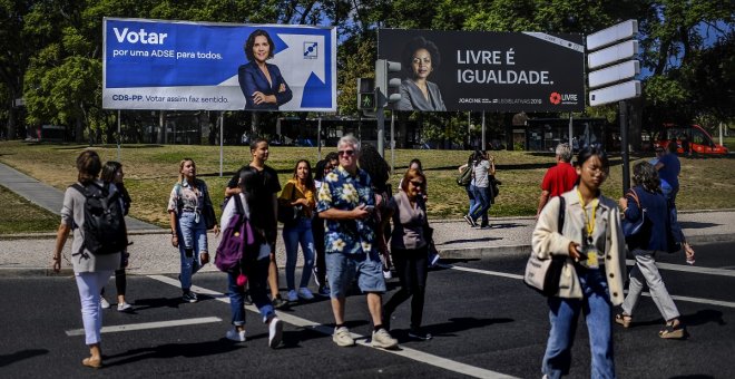 01/10/2019 - Personas cruzan una calle en Portugal ante pancartas electorales. / AFP - PATRICIA DE MELO MOREIRA