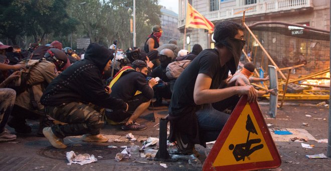 Varios jóvenes encapuchados se protegen de las balas de goma con un parapeto de cartón y cinta de embalaje, durante los disturbios de Barcelona. GUILLEM SANS