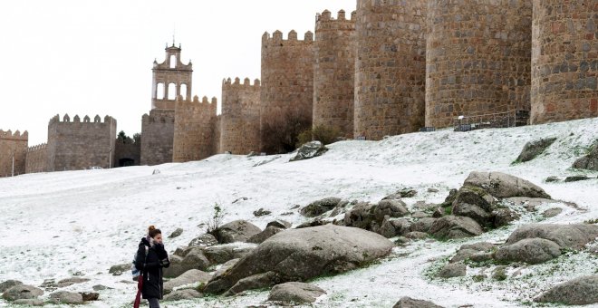Una mujer camina junto al lienzo norte de la muralla de Ávila cubierta por una fina capa nieve caída en las últimas horas. EFE