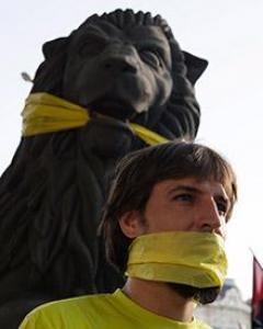Un manifestante, con la boca tapada junto a la figura de un León amordazado.- SERGIO PÉRES (REUTERS)