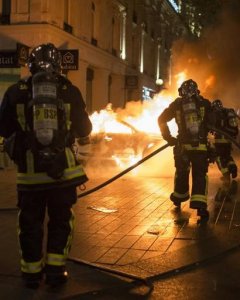 Bomberos tratan de apagar las llamas de un coche de Policía incendiado. - AFP