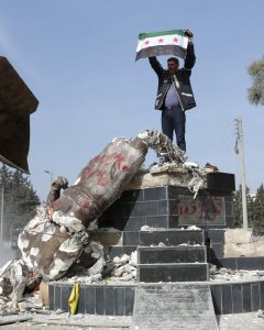 Miembro del Ejército sirio libre respaldado por Turquía sostiene una bandera mientras derriban la estatua kurda en el centro de Afrin, Siria. REUTERS