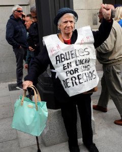 Una jubilada que porta un peto con un mensaje reivindicativo levanta el puño al ver pasar la marcha | Chema Moya / EFE