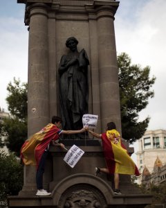 Varias personas escalan las esculturas de la Plaza de Catalunya de Barcelona para colocar una bandera española durante la manifestación convocada por Societat Civil por el día de la Fiesta Nacional. REUTERS/Juan Medina