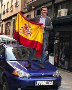 Pablo Casado posando con una bandera de España sobre el capó de un coche como parte de la campaña de primarias del PP.