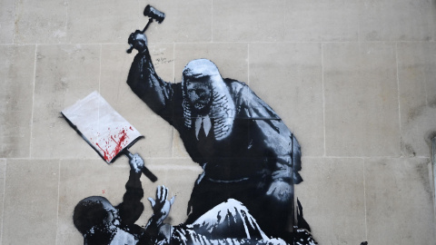 La obra de Banksy representa a un juez golpeando con un mazo a un manifestante que se protege con una pancarta.