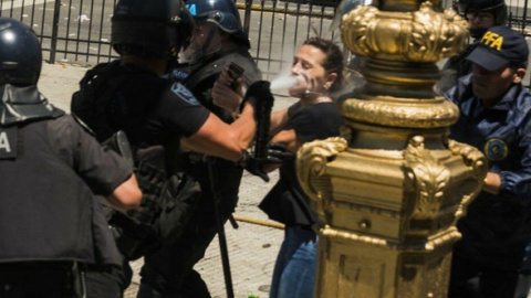 Una diputada nacional, con su credencial en alto, reclama a las fuerzas de seguridad el cese de la represión desatada contra los manifestantes. Un efectivo le responde arrojándole gas pimienta directamente al rostro, provocándole quemaduras graves.