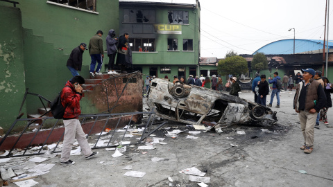 Ciudadanos caminan junto a un coche calcinado en El Alto, Bolivia. / Reuters Ciudadanos caminan junto a un coche calcinado en El Alto, Bolivia. / Reuters