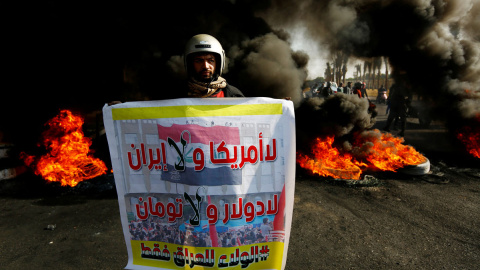 Un manifestante iraquí lleva un cartel que dice: "No Estados Unidos ni Irán, No dólar y No Toman, lealtad solo a Irak" junto a la quema de neumáticos para bloquear una carretera durante las protestas contra el gobierno en Najaf. REUTERS / Alaa al-Mar Un manifestante iraquí lleva un cartel que dice: "No Estados Unidos ni Irán, No dólar y No Toman, lealtad solo a Irak" junto a la quema de neumáticos para bloquear una carretera durante las protestas contra el gobierno en Najaf. REUTERS / Alaa al-Marj