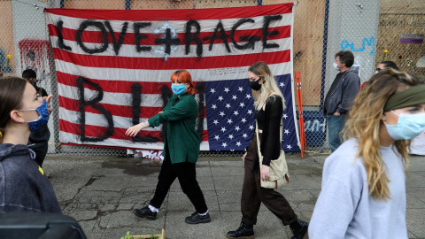 Varias personas pasan por delante de una bandera estadounidense vuelta del revés, en protesta contra el racismo, en el edificio del Recinto Este del Departamento de Policía de Seattle, en la autoproclamada Zona Autónoma de Capitol Hill. REUTERS / Gora Varias personas pasan por delante de una bandera estadounidense vuelta del revés, en protesta contra el racismo, en el edificio del Recinto Este del Departamento de Policía de Seattle, en la autoproclamada Zona Autónoma de Capitol Hill. REUTERS / Goran